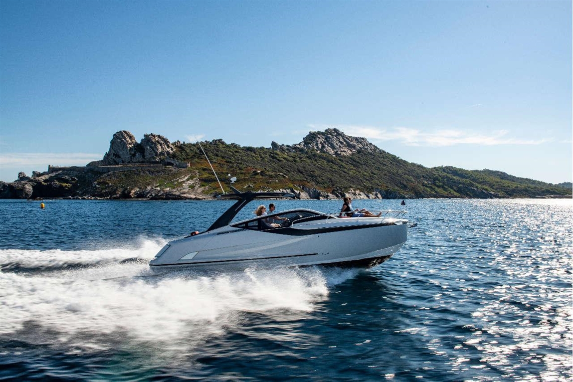 A sleek white motorboat speeds across sparkling water near rocky hills, with passengers enjoying the scenic ride.